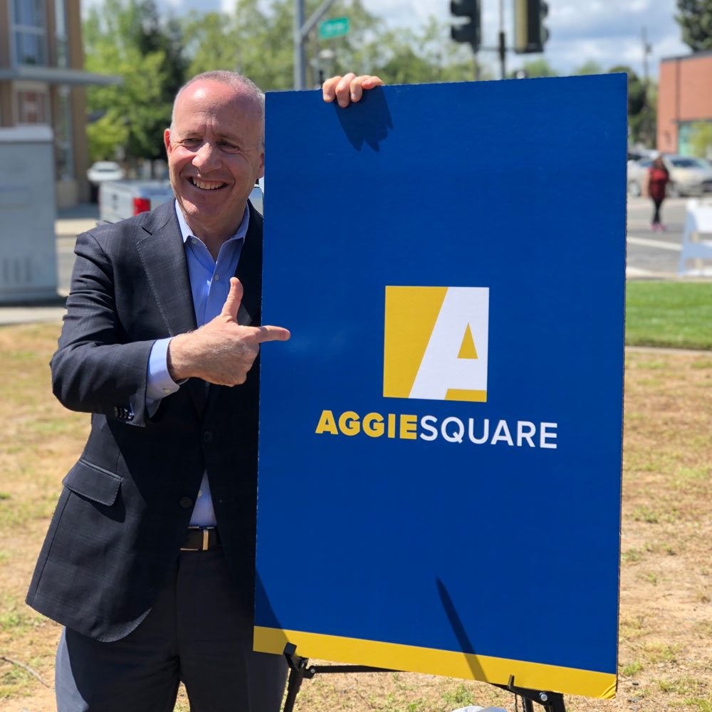"A picture of a man pointing to a sign that says Aggie Square"