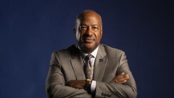 A portrait of Chancellor Gary May with crossed arms in front of a dark blue background