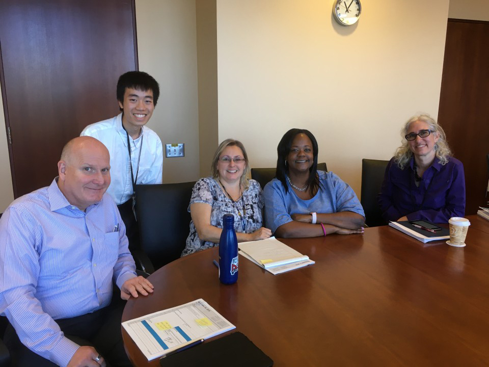 A group of five people smile and look at the camera during a meeting