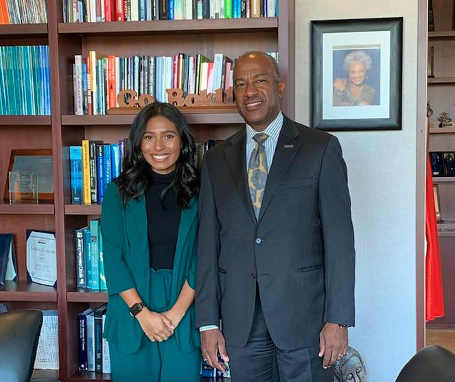 Two people stand with book shelves behind them