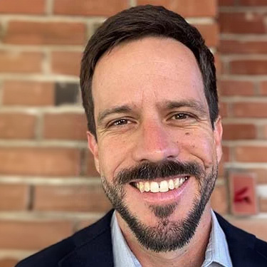 Man with beard smiles in front of brick background