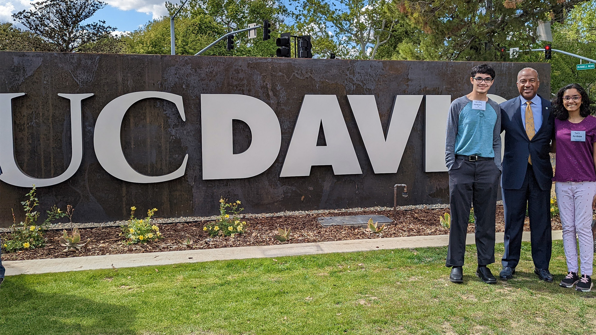 Tanishq Abraham and Tiara Abraham pose for a photo with Chancellor Gary S. May at the new UC Davis sign.