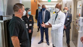 Chancellor Gary May and other leaders stand and watch a UC Davis Health staff member in a white lab coat speak with other staff members