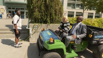 Chancellor May and the provost drive an ATV while laughing with a student. 