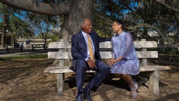 Photo of Chancellor Gary May and LeShelle May talking and laughing while sitting on a wooden bench outside