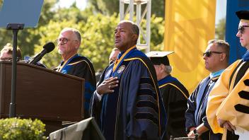 Photo of Chancellor Gary May at commencement with his hand on his chest as a student sings the national anthem out of frame
