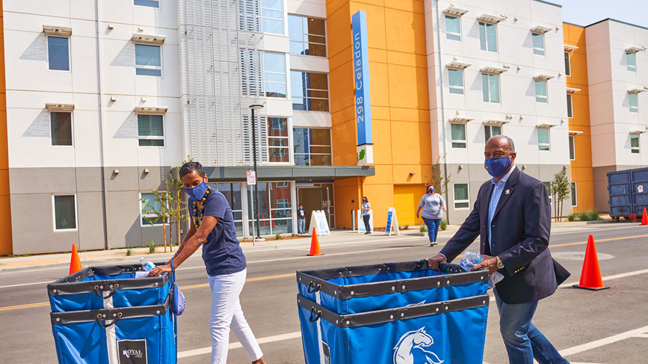 Chancellor May and Leshelle in front of The Green residence halls pushing carts