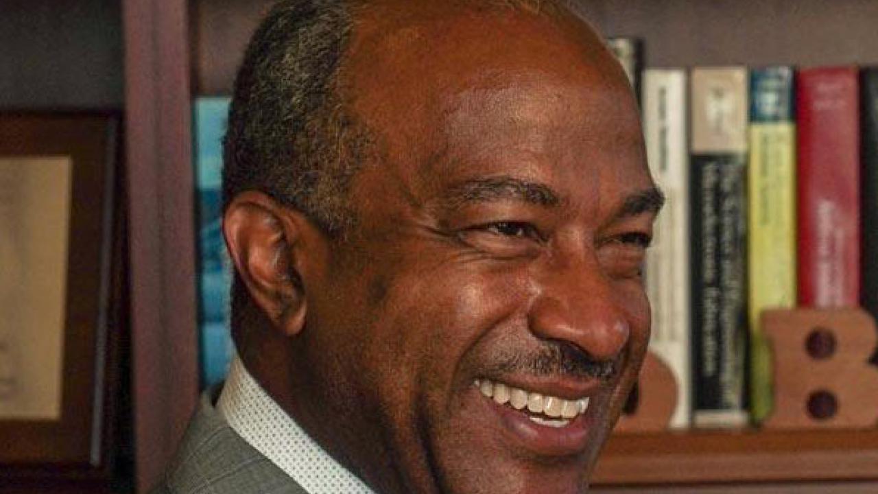 Chancellor May looking to the right of the frame smiling in front of a full bookcase.