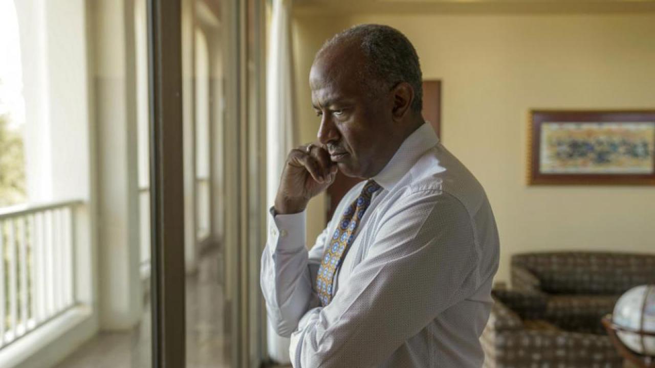 Chancellor Gary S. May stands, a hand on his chin.