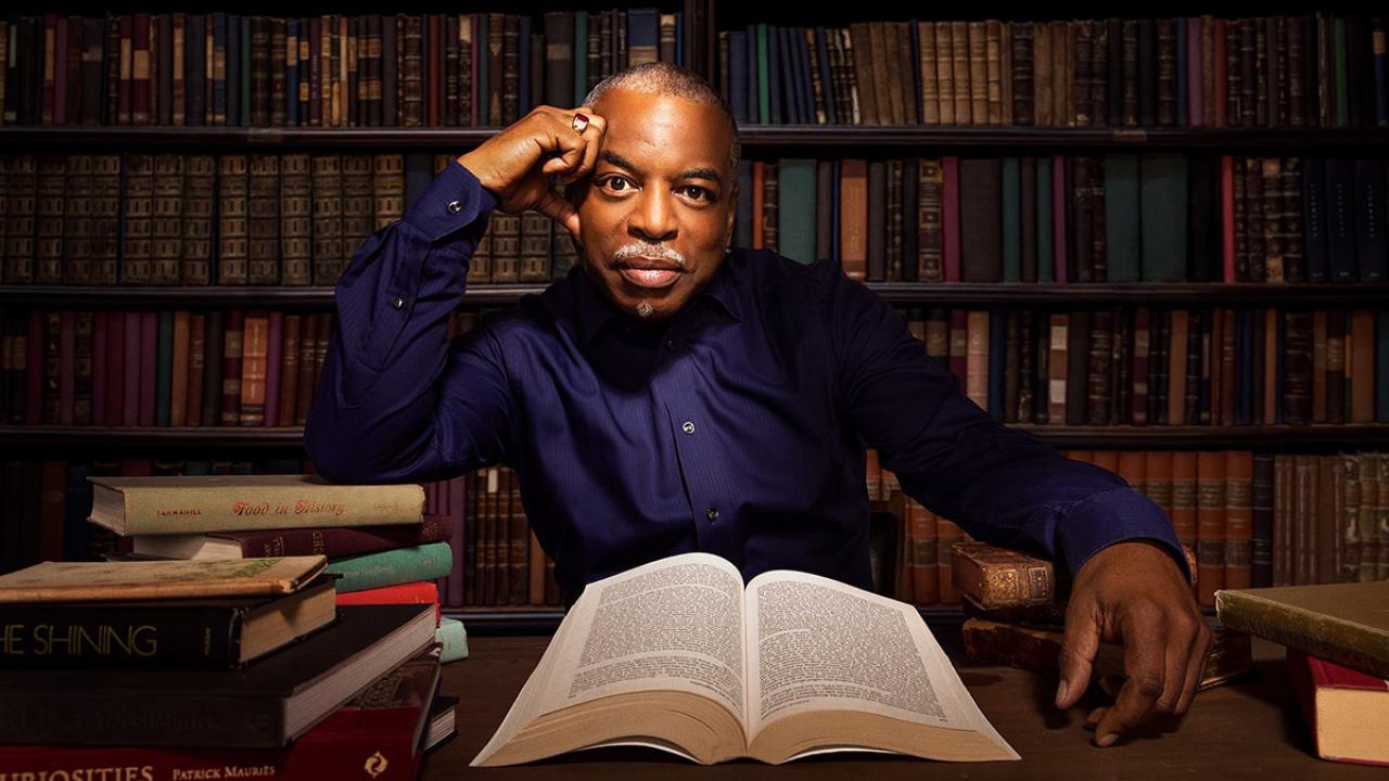 Photo of LeVar Burton in a library, surrounded by books. 