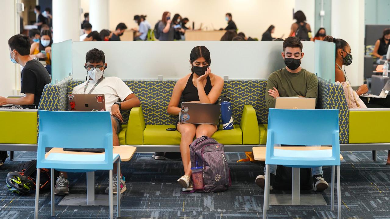 Three students with masks on use their  laptops while sitting on a couch in the Memorial Union.