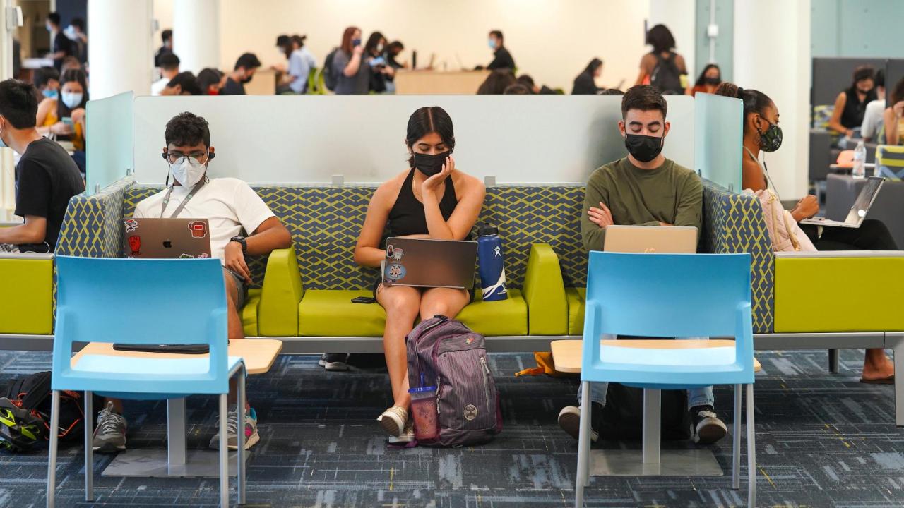 Three students with masks on use their  laptops while sitting on a couch in the Memorial Union.