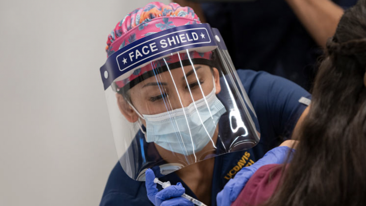 Healthcare worker with face shield giving COVID vaccine to patient