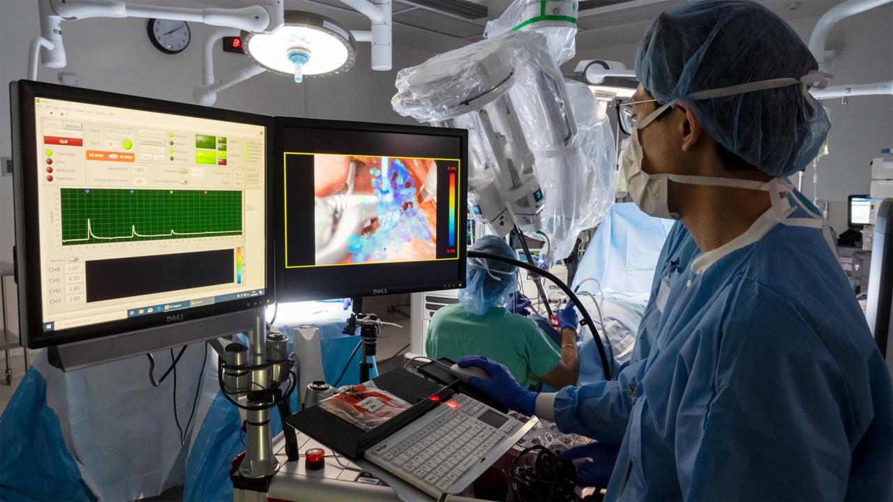 A surgeon wearing blue scrubs is looking at a monitor screen. 