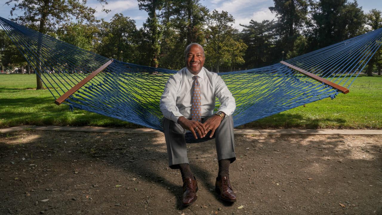 Chancellor Gary S. May, in shirt and tie, seated on hammock on the Quad.