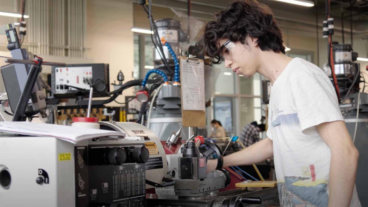 A student in a white T-shirt working on equipment in an engineering lab.
