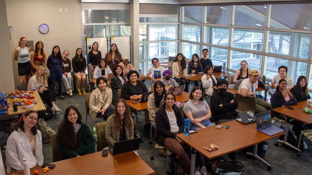 Group of about 30 students and instructors smiling in a bright classroom with laptops.