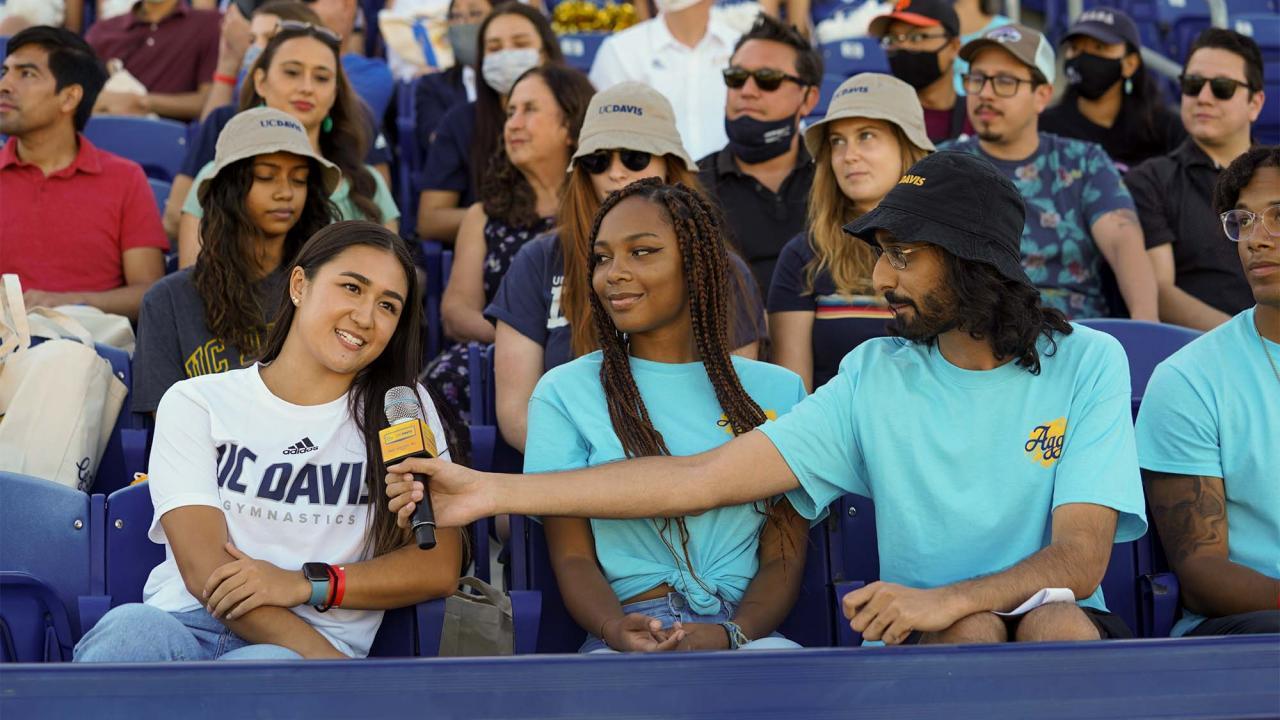 Student Gauruv Virk holds microphone to interview students at stadium.