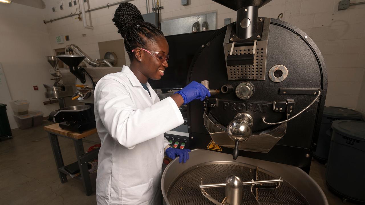 Woman in lab coat works with large coffee roaster