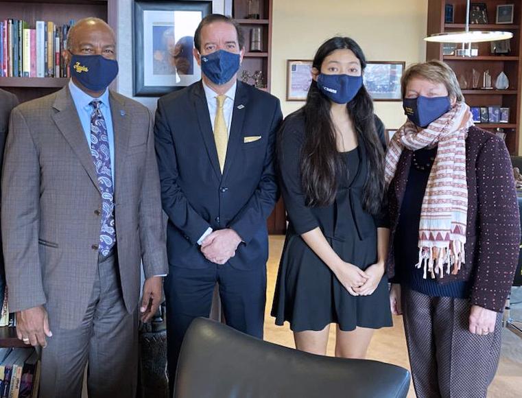Four people standing, looking at the camera, wearing COVID masks