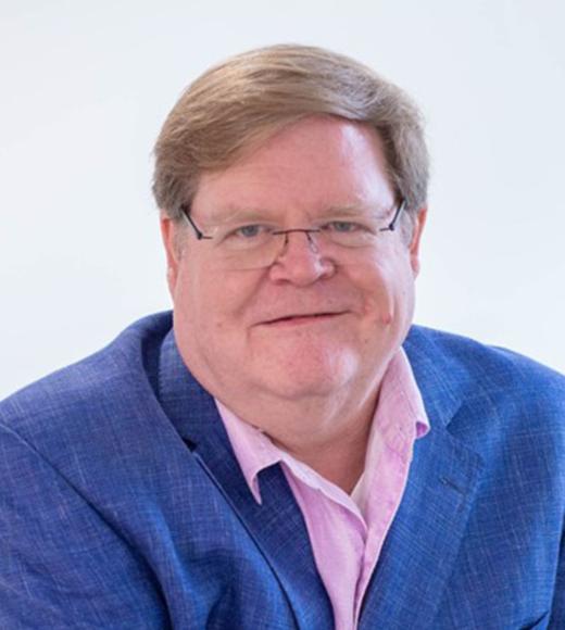 Smiling older man wearing glasses, blue blazer and pink shirt against white background