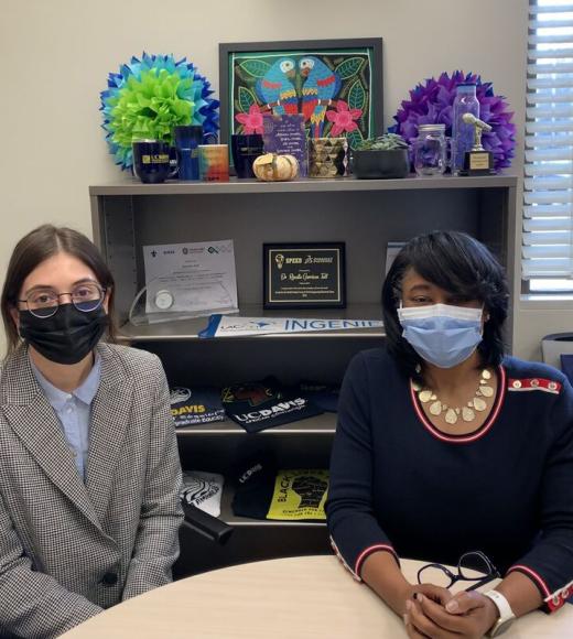 Two people with masks pose at an office table