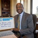 Chancellor Gary May looks into the camera smiling, holding a dry erase board that says, "I stand with undocumented students because they deserve justice and the opportunities all Americans enjoy".
