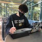 Student with mask working on laptop and tablet with UC Davis sweatshirt