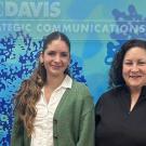 Two people pose for photo in front of blue wall with plaque: UC Davis Office of Strategic Communications