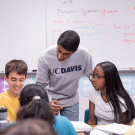 A standing student with a UC Davis shirt works with elementary age students.